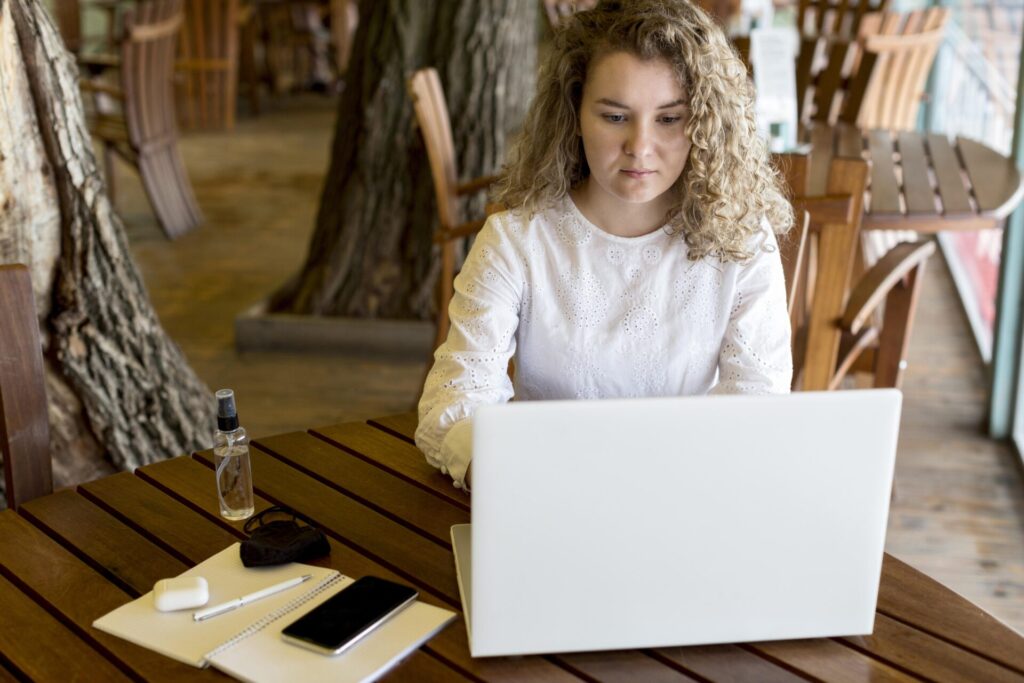 Дівчина-початківець працює з ноутбуком обираючи хостинг для портфоліо на терасі